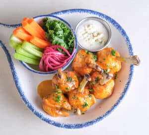 Photo of six chicken lollipops on plate with golden BBQ sauce, carrot, celery, blue cheese.