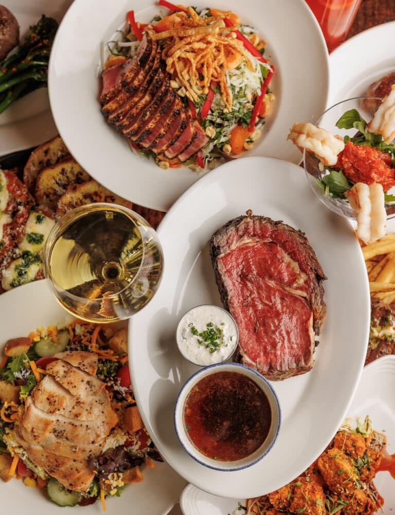 steak, fish, a glass of wine and other dishes on a table